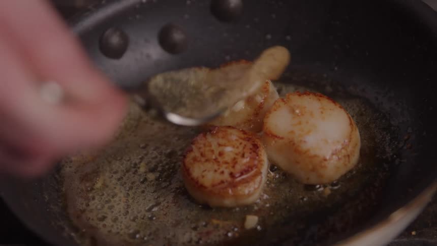 Scallops searing in hot butter inside the pan