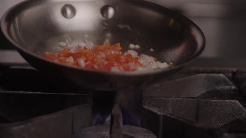 Pan heating a mix of onions and bell peppers over the stove flame