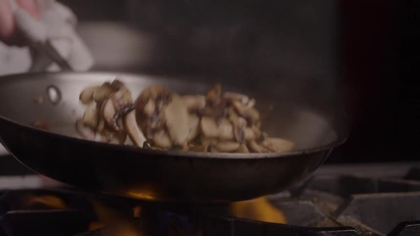 The chef is cooking sliced mushrooms in the pan