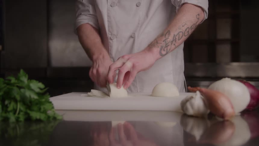 Cook chopping onions on the cutting board beside fresh seasonings