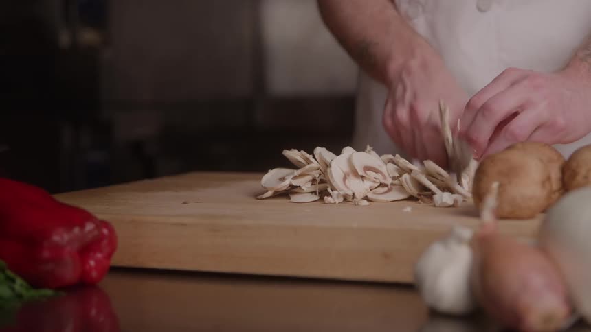 Close up of a male chef slicing potatoes on a chopping board in the kitchen during daytime