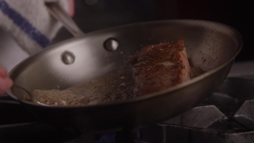 Butter being spooned over steak as it cooks in the hot pan