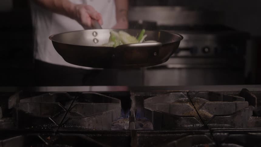 The chef is flipping vegetables in the pan