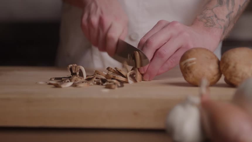 Hands slice mushrooms on a wooden cutting board in the kitchen