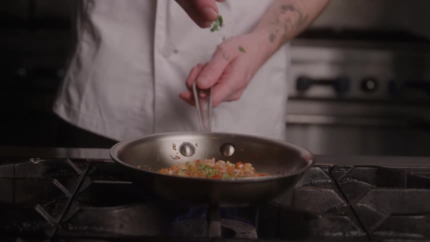 The chef sprinkles herbs on the pan full of vegetables
