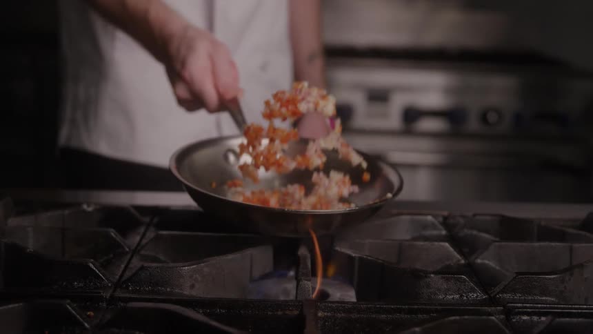 Male chef jiggles a frying pan while cooking diced vegetables in a restaurant kitchen