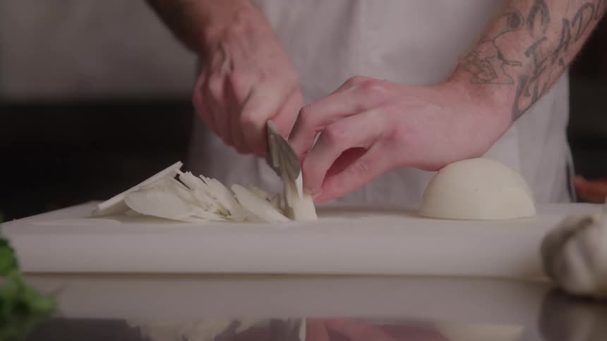 Cook slicing white onion into thin strips on the cutting board
