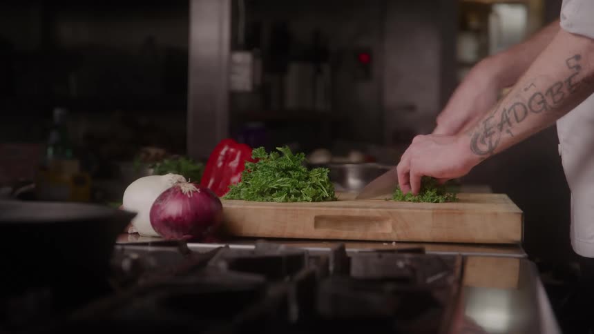 Cook chopping fresh parsley beside vegetables on the counter