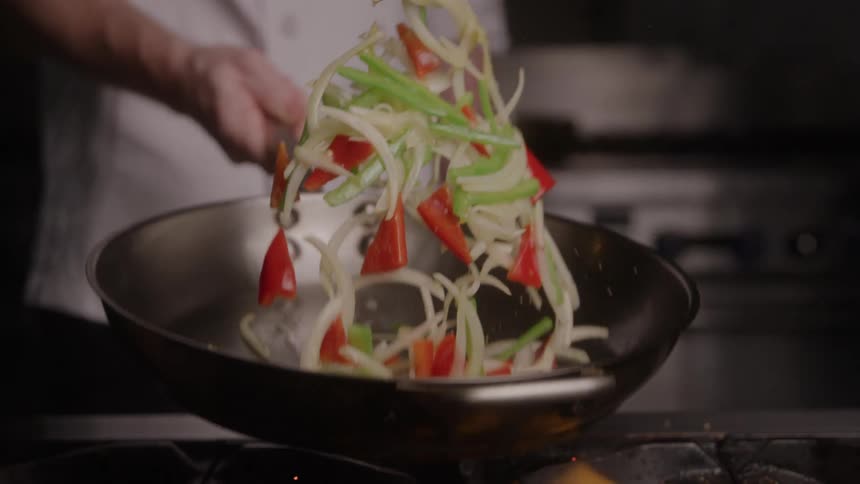 Cook frying vegetables holding the frying pan over the fire on the stove