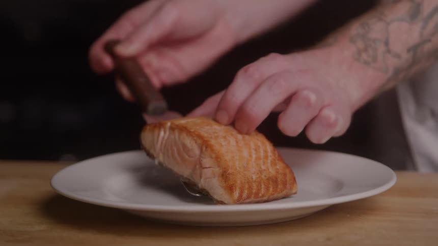 Grilled salmon is placed on the plate with the help of a spatula
