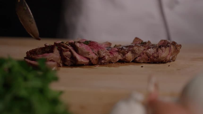 Sliced steak being topped with a spoonful of sauce on the board