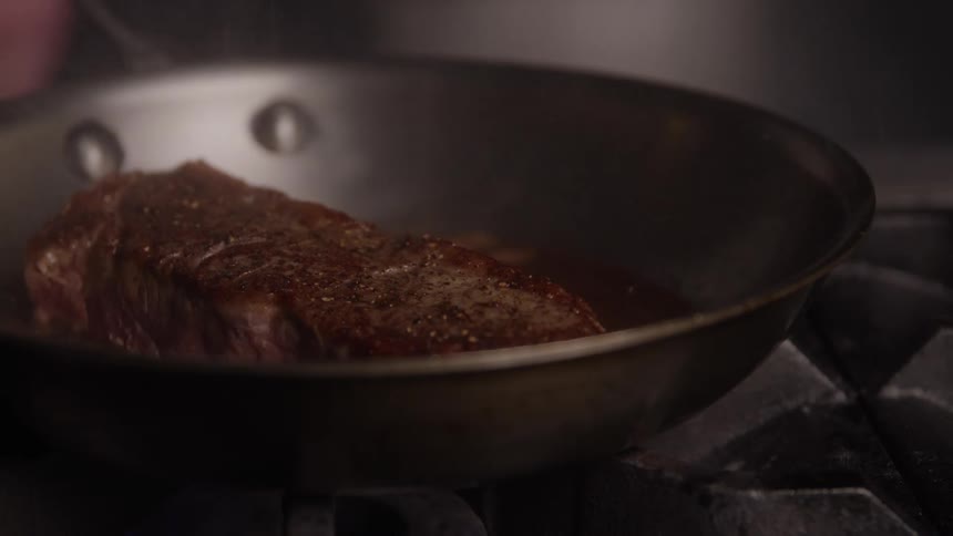 Person cooks a steak in a frying pan sitting on a gas stove top