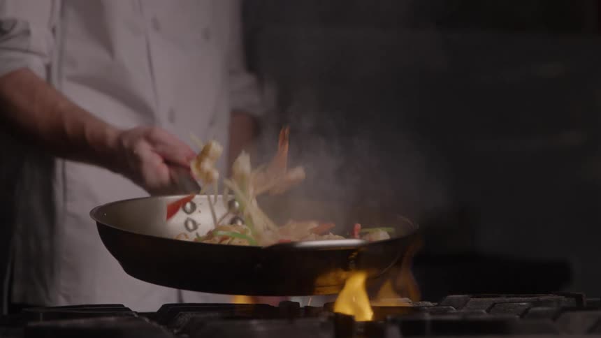 Close up of a male chef sauteing food in a frying pan while cooking in the kitchen