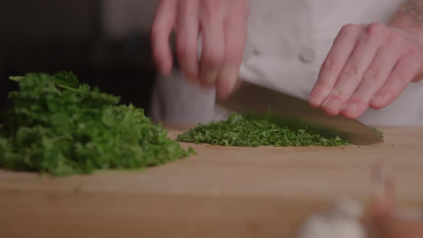 Cook finishing the chop of parsley into small pieces on the board