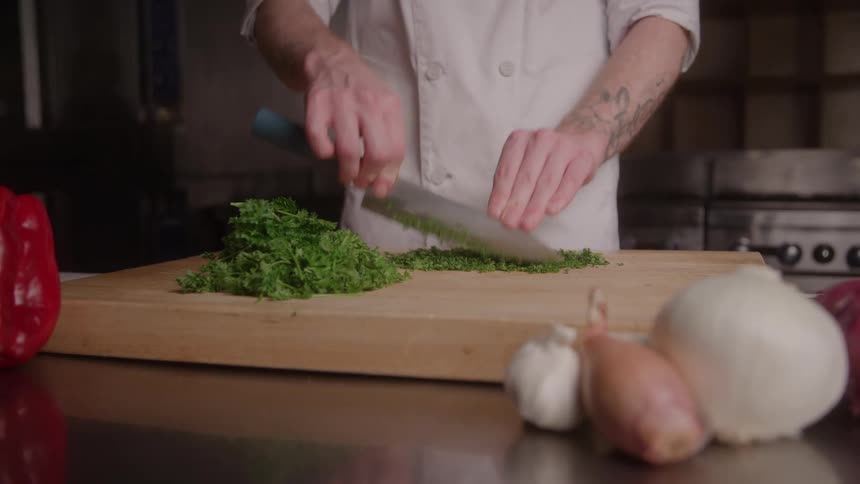 A person using a knife to cut a green vegetable into many small pieces