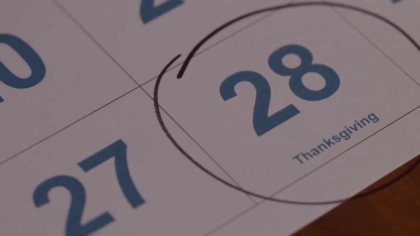 A close up of a persons hand circling date 28 thanksgiving with a black marker on a paper calendar