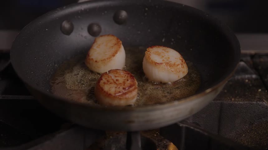 Scallops searing in the pan with melted butter