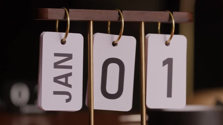 A hand slides a wooden calendar with three white hanging cards displaying a date clearly showing jan 01 in bold dark text