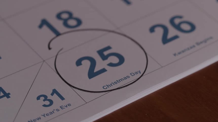 A hand holds a black marker and quickly draws a circle around the number 25 labeled christmas day on a paper calendar