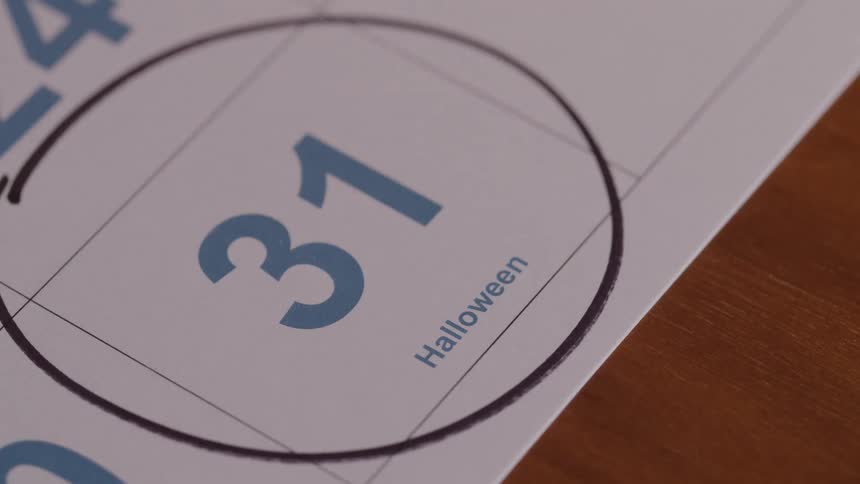 Persons hand holding a pen draws a circle around halloween the 31st on a calendar