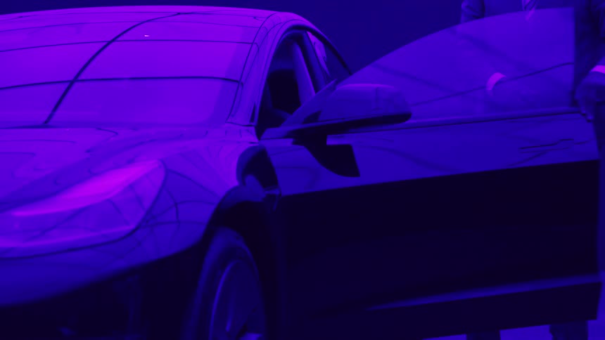 Man gets out of a black sports car parked in a garage with purple light