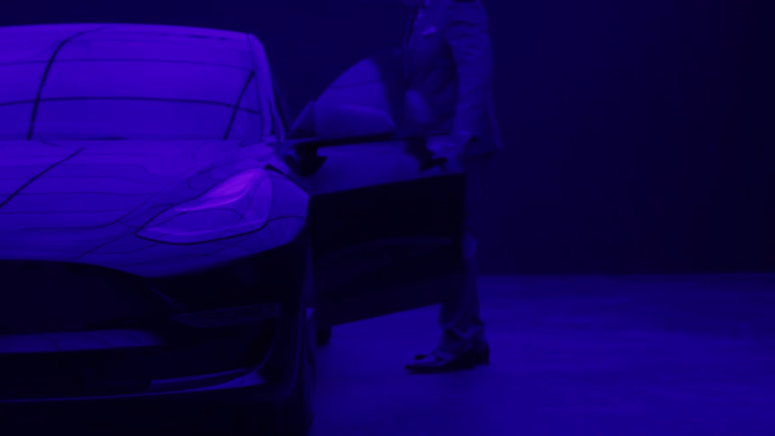 A middle aged black male executive walks and enters his car parked in a blue lit garage