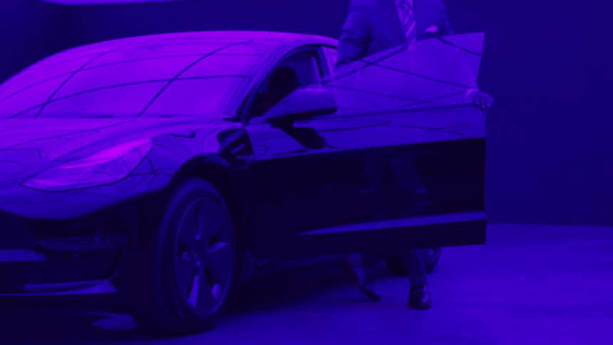 Man gets out of a black sports car parked in a garage with purple light