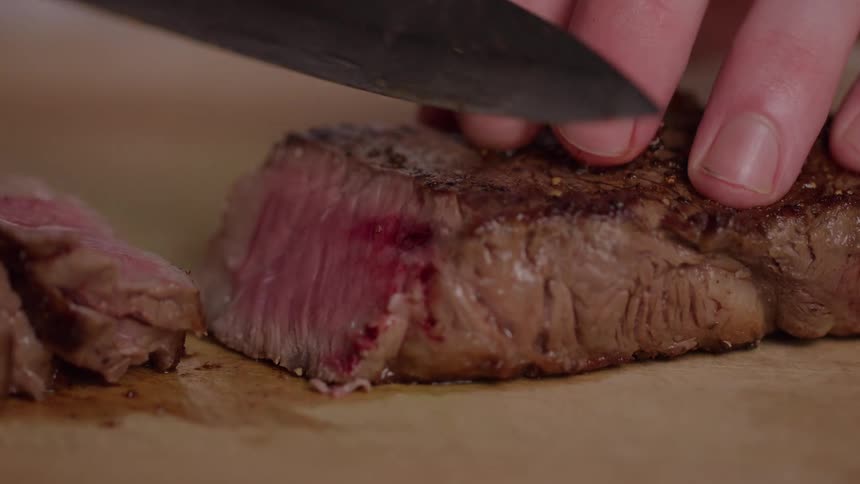 Cook holds meat with his fingertips as he slices it with a knife