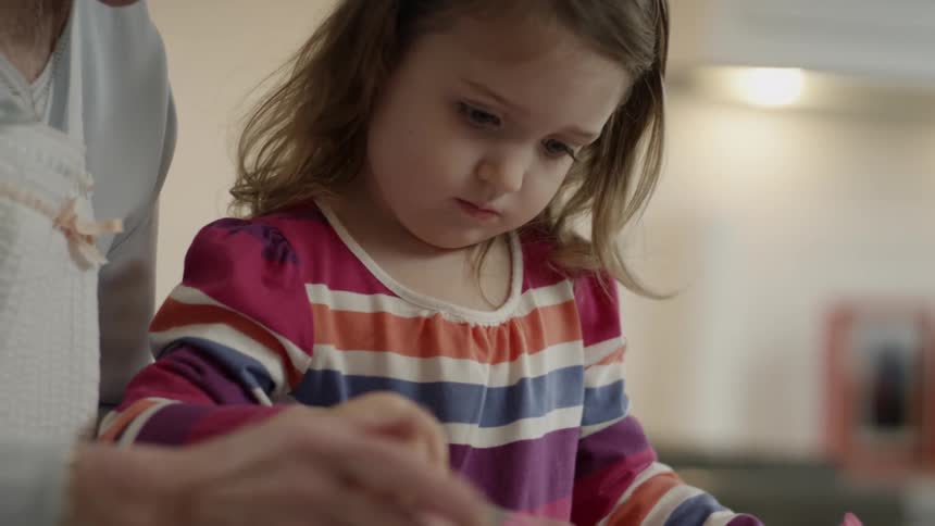 Older woman holding cupcake while little girl spreads pink frosting on it