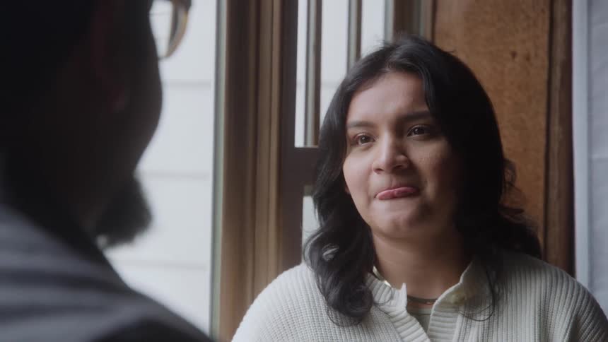 Awoman looks intently forward smiling partially obscured by the large white mug being raised to the mouth of a darkhaired man in the foreground suggesting a focused conversation