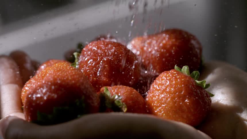 Strawberries being rinsed under running water while resting in the hands
