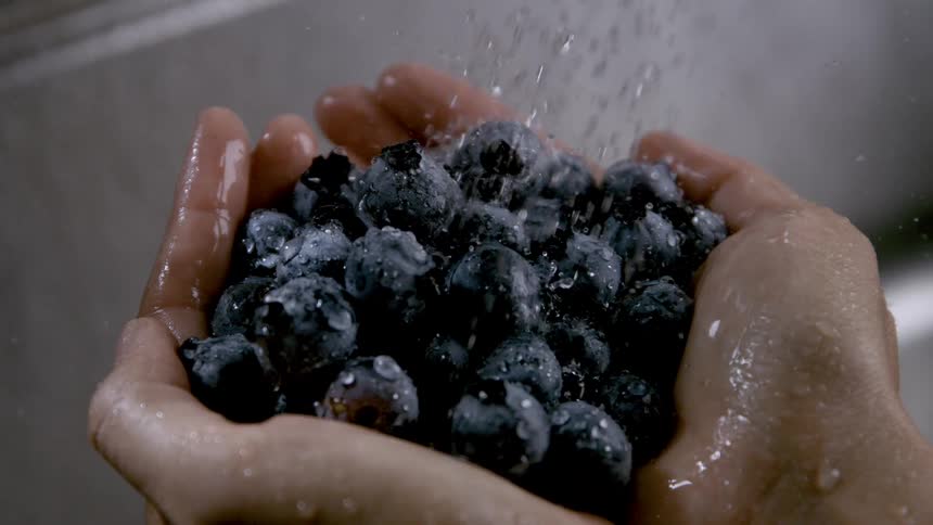 Close up a person washing blueberries under a running faucet during daytime