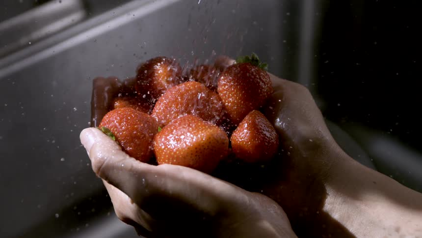 Close up of a person holding strawberries under a running faucet to wash them indoors