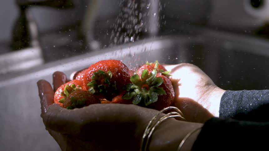 Strawberries being rinsed in the hands under a strong stream of water