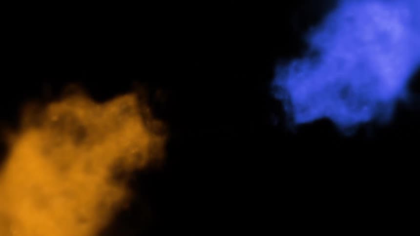 Two distinct billowing plumes of intensely colored smoke stream from the left and right sides of the frame one blue and the other orange converging and dissipating against a pure black background