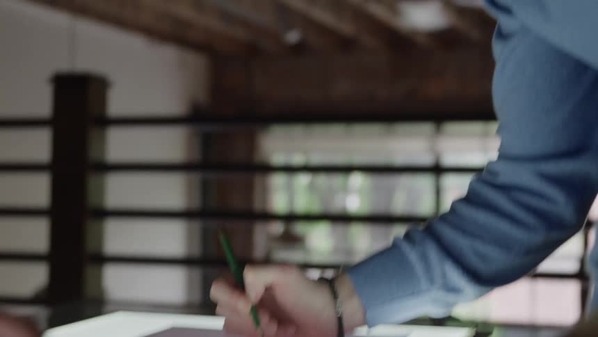 Person drawing on a lighted desk while another watches nearby