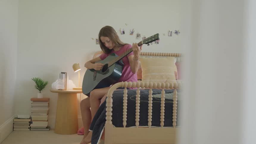 Teenage girl sitting on her bed playing an acoustic guitar
