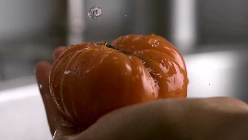 Water from a faucet drips onto a tomato in a womans hand