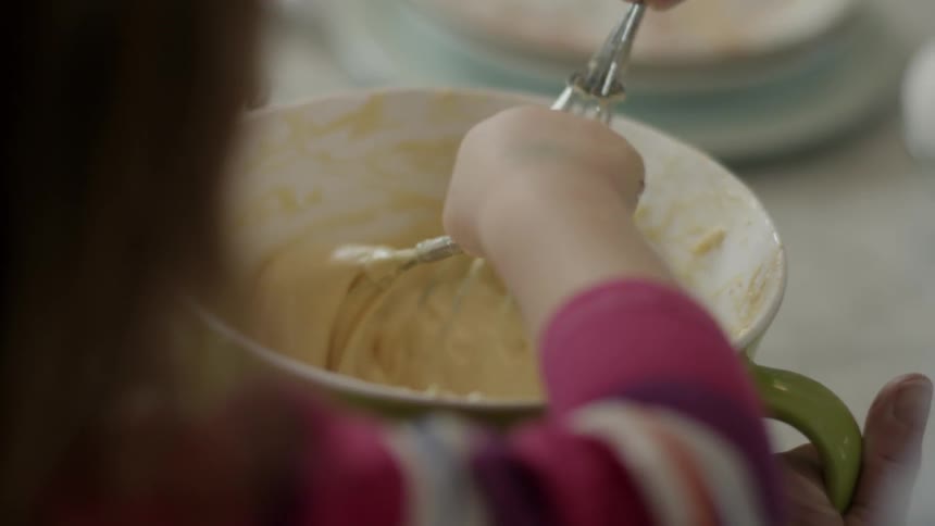 Person and child stirring batter in a glass bowl