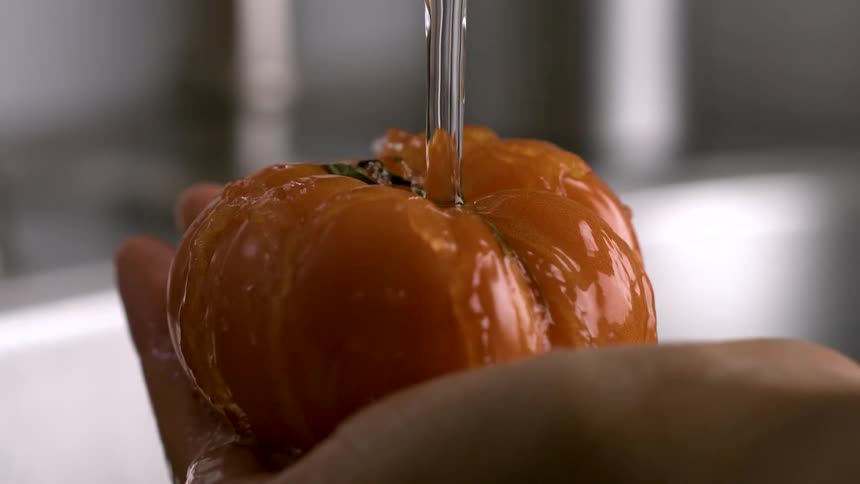 Water from a faucet falls onto a tomato in a womans hand