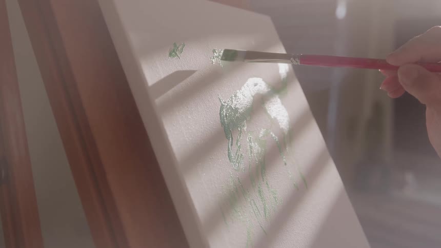 Brush adding green strokes to a sunlit canvas