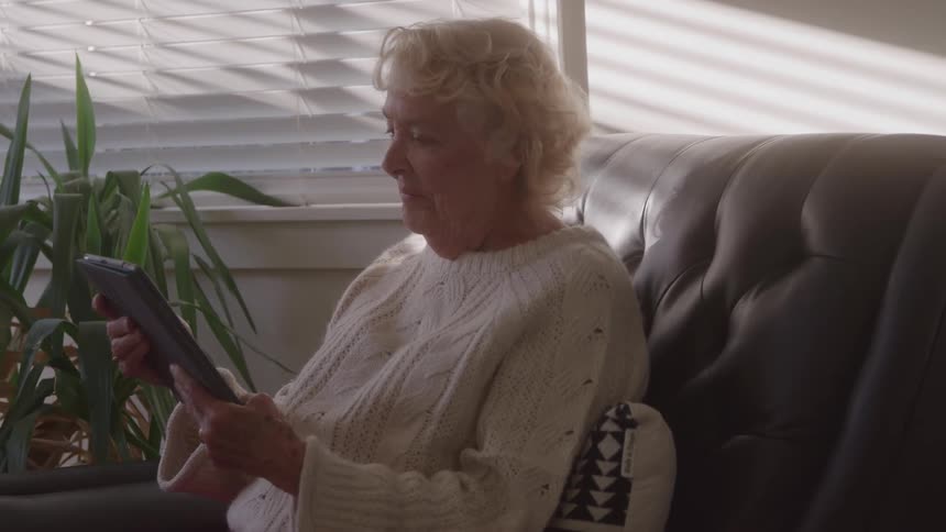 Elderly woman sitting on the couch holding a tablet and smiling