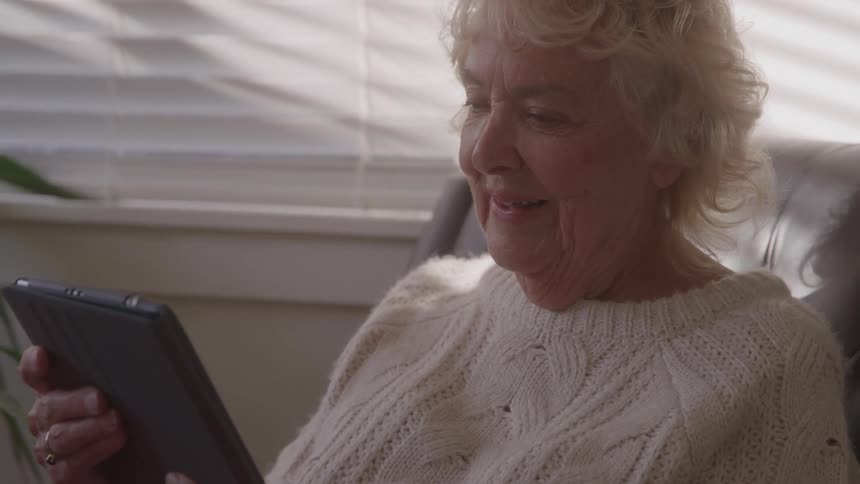Elderly woman smiling while holding a tablet