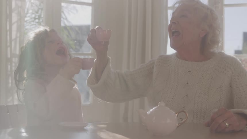 Elderly woman and child clinking small cups at the table
