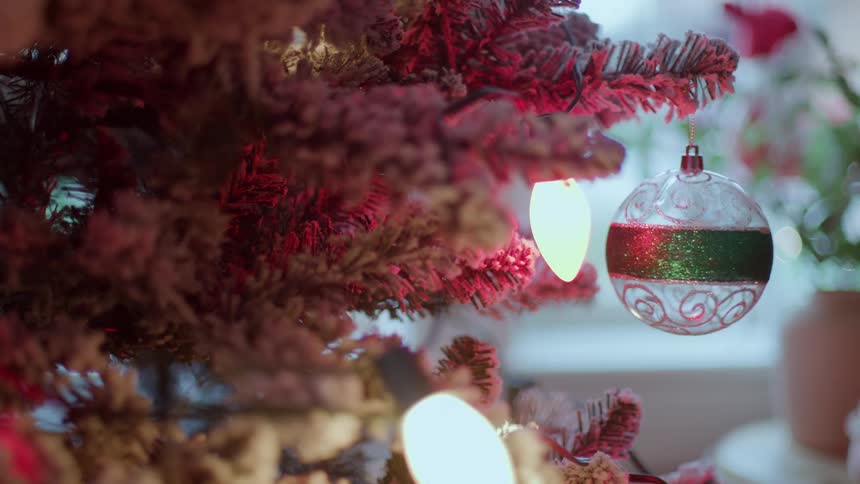 A festive glittery ornament hangs on a frosted christmas tree illuminated by warm glowing lights