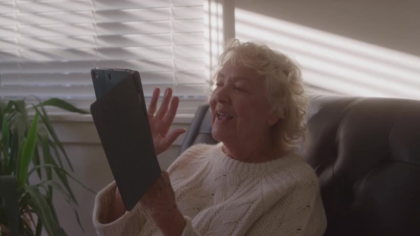 Elderly woman waving while talking over video on her tablet