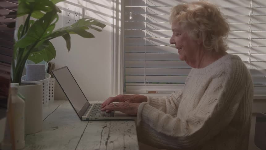 An old woman types on a laptop
