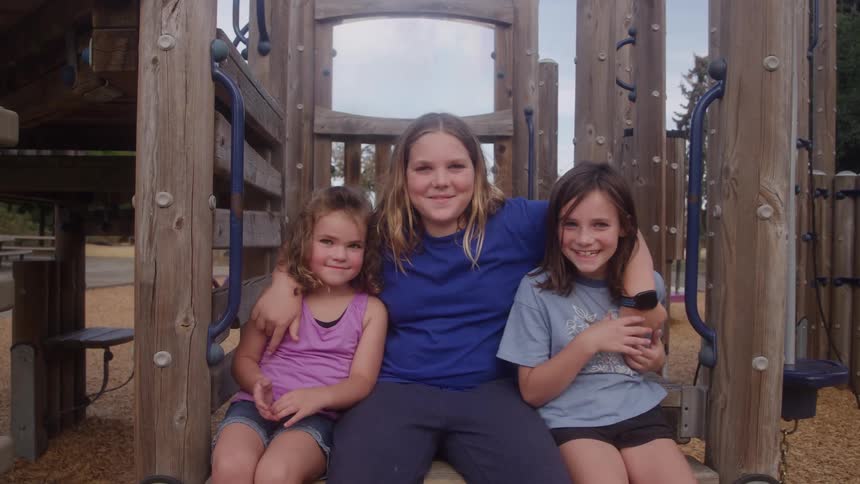 Three children sitting together on wooden playground structure showing friendship in outdoor setting