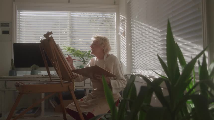 An old woman paints a canvas