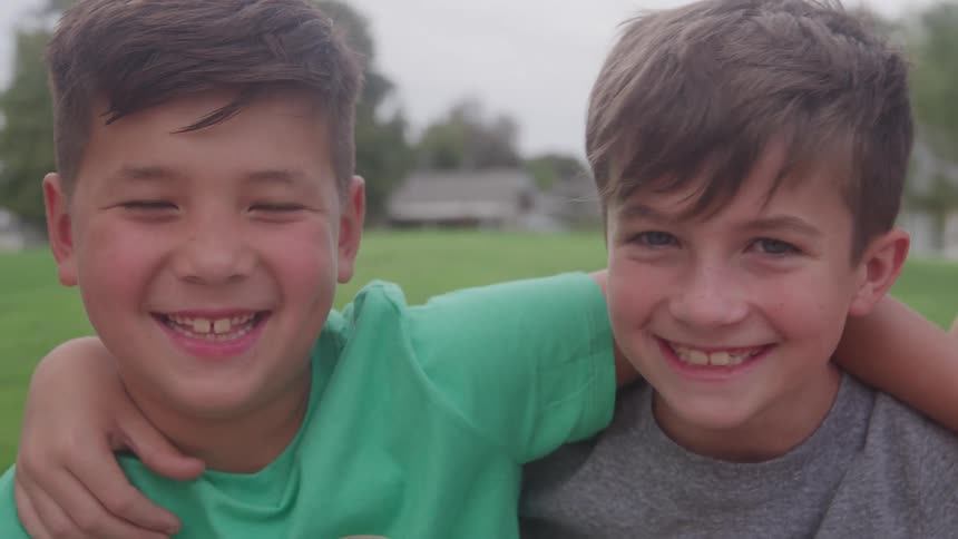 Two boys hanging out together in a field with thier arms around each others shoulders